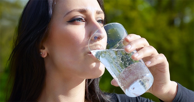 A woman drinking a glass of carbonated water | Trainest