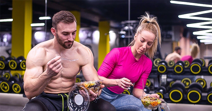 Two fit people eating salad inside a gym | Trainest