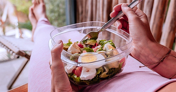 A woman eating a bowl salad | Trainest