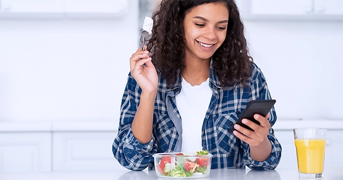 A woman eating while looking at her phone | Trainest