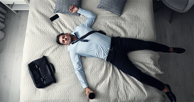 An exhausted office worker lying in bed | Trainest