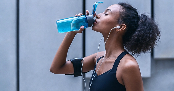 Someone in gym clothes drinking water | Trainest