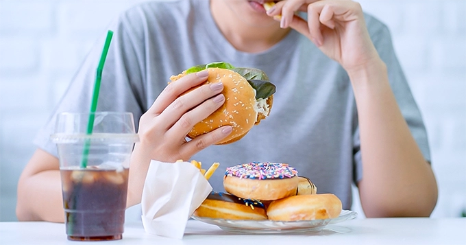 Someone binge-eating junk food | Trainest