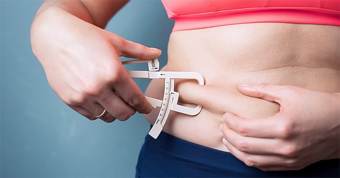 A woman using a skinfold caliper | Trainest