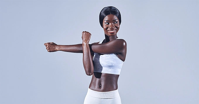 A woman in gym attire stretching | Trainest