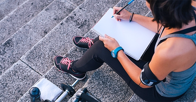 A woman in gym clothes writing | Trainest 