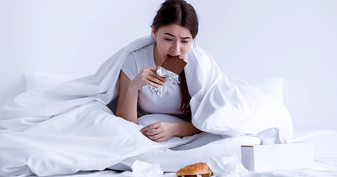 A woman eating junk foods in bed | Trainest 