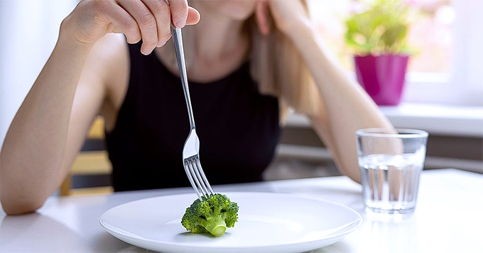 A woman eating a single piece of broccoli | Trainest 