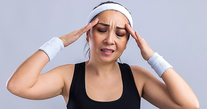 A lady in gym clothes having a headache | Trainest
