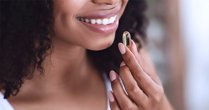 A woman taking a softgel capsule | Trainest 