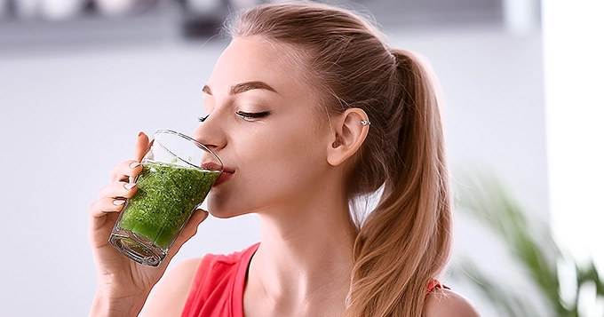 A woman drinking a glass of detox juice | Trainest 