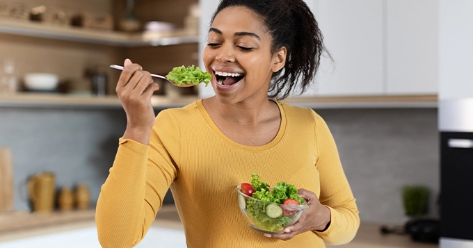 A woman having a salad in the kitchen | Trainest 