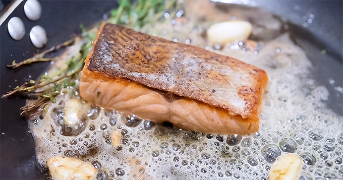 A parcel of salmon being pan-fried | Trainest 