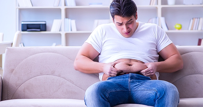 A slightly overweight man holding his stomach fat | Trainest 