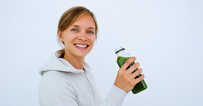 A fit person wearing gym clothes and drinking a green-colored smoothie | Trainest 