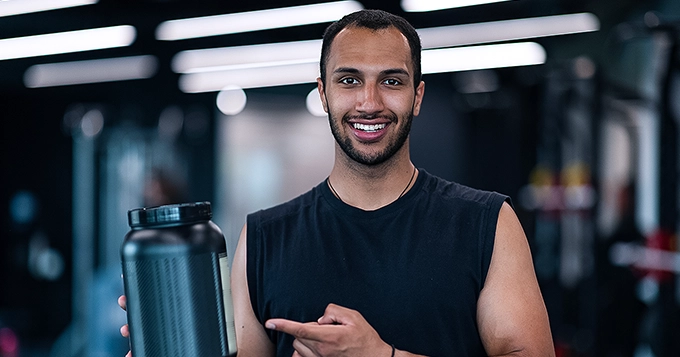 A person in a gym pointing to the nutrition label of a fitness supplement | Trainest 