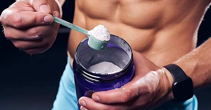 A muscular man scooping out of a powdered-supplement tub | Trainest 