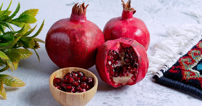 A bowl of pomegranate seeds and whole pomegranates | Trainest 