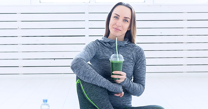 A woman in gym clothes drinking a smoothie | Trainest 