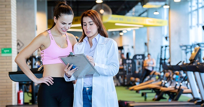 A health expert showing a chart to a client in the gym | Trainest 