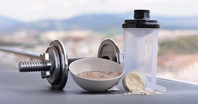 Servings of protein powder, a shaker bottle, and a dumbbell | Trainest 