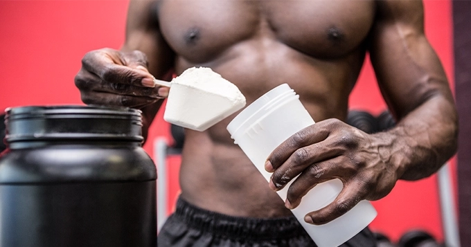 A jacked man scooping protein powder into his shaker bottle | Trainest 