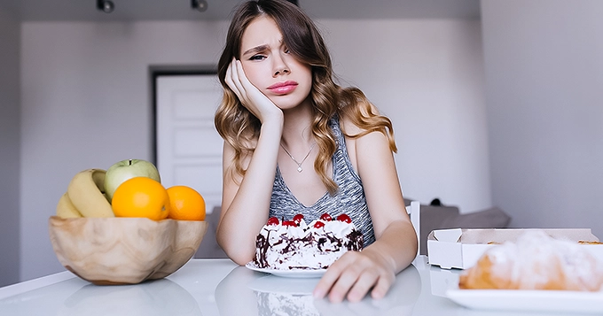 A young woman looking disgruntled in front of food | Trainest 