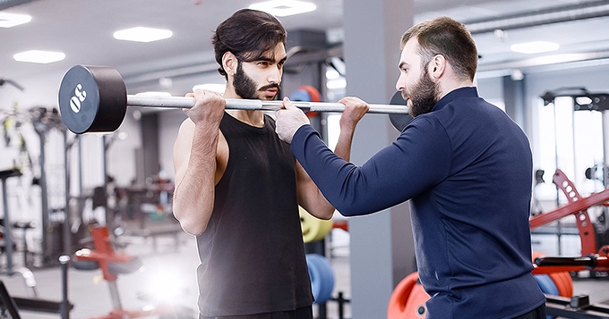 A man curling a barbell with a spotter | Trainest 