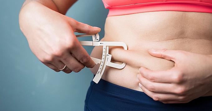 A woman using a body fat caliper on her waist | Trainest 