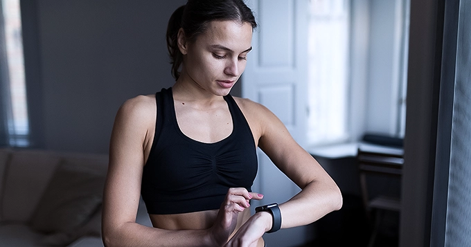 A fit woman in workout clothes looking at her smartwatch | Trainest 