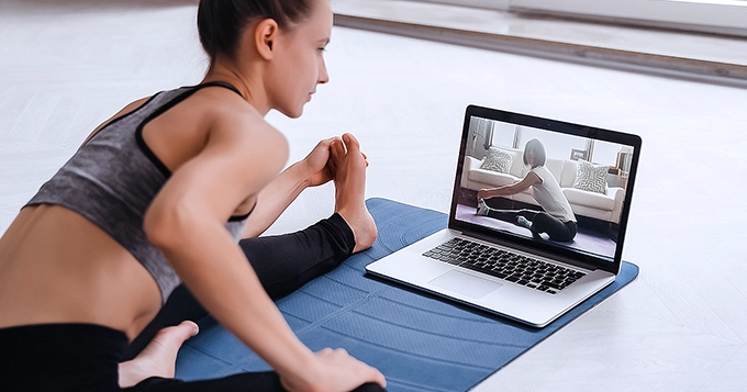 A woman exercising on the floor in front of a laptop | Trainest 