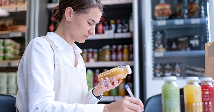 A woman examining the nutrition label of a drink in a supermarket | Trainest 