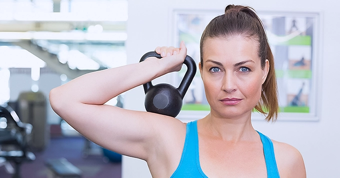 A woman lifting a kettlebell with one hand | Trainest
