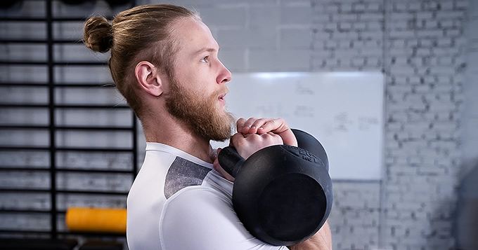 A fit man doing kettlebell double rack carries | Trainest
