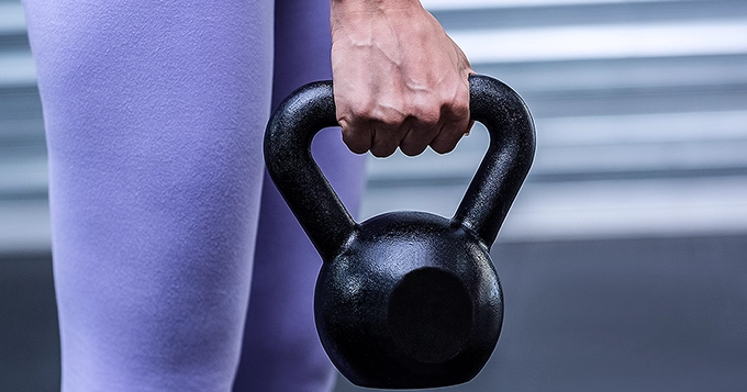 A close-up of a hand holding a kettlebell by the handle | Trainest
