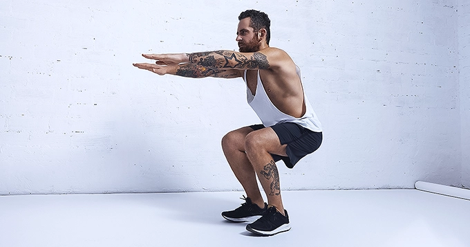 A tattooed man doing air squats | Trainest 