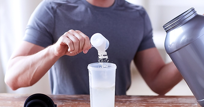 Someone scooping protein powder into a protein shaker bottle | Trainest 