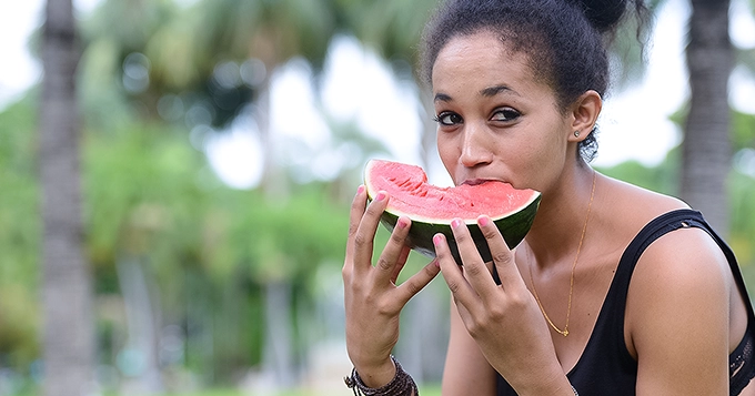 A woman outdoors, eating a slice of watermelon | Trainest 