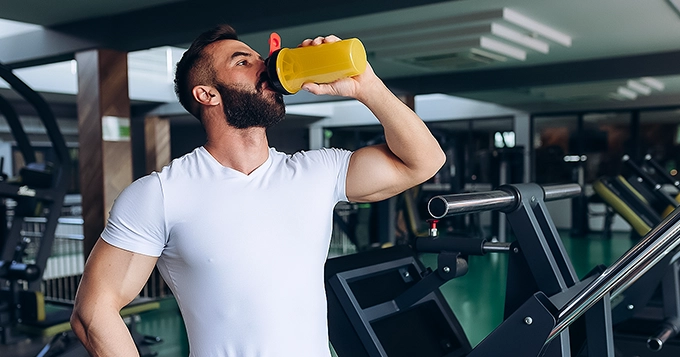 A muscular man drinking from a shaker bottle | Trainest 