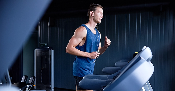 A fit dude running on a treadmill in a commercial gym | Trainest 