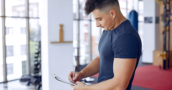 A gymgoer writing something down on a clipboard in a gym | Trainest 