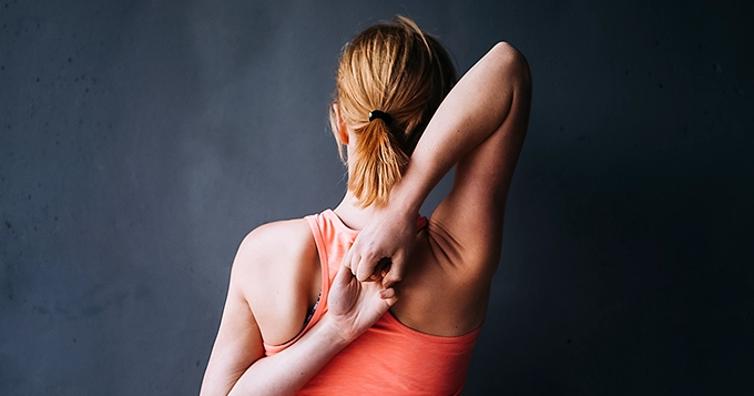 A woman doing back stretch with arms touching from the back | Trainest