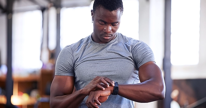 A fit man in the gym looking at his smartwatch | Trainest
