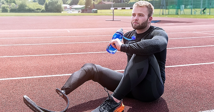 A runner with a prosthetic leg resting on the track | Trainest 