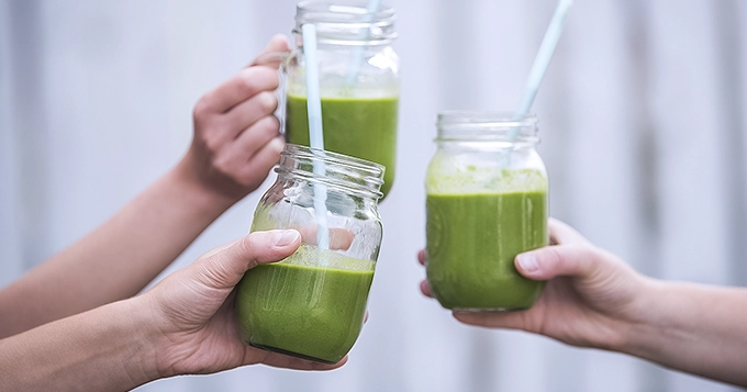 People holding mason jar mugs of green tea smoothies | Trainest 