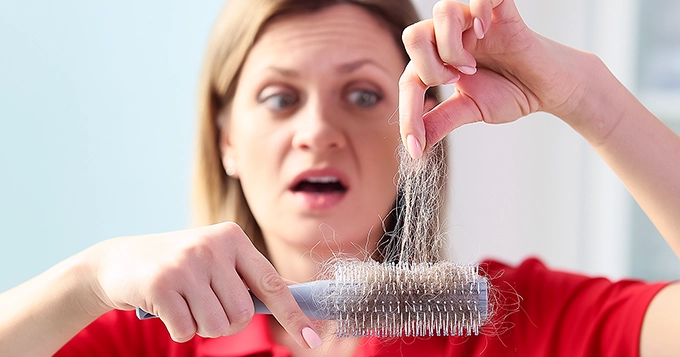 A woman holding a hairbrush with hair stuck onto it | Trainest 