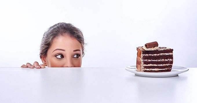 A woman behind the table looking at a piece of cake | Trainest 