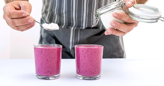 Someone spooning powder into a glass of smoothie | Trainest 