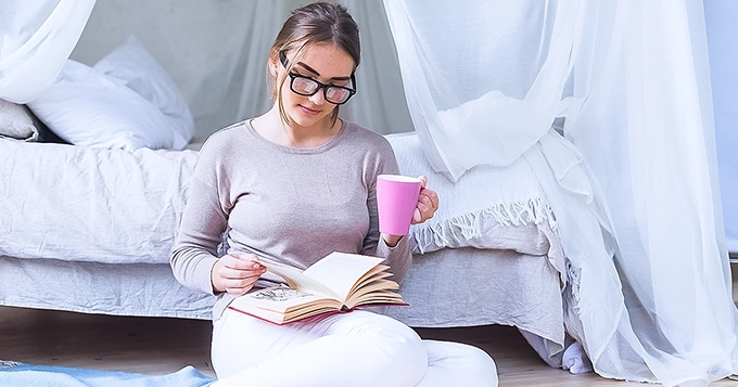 A young woman reading a book by her bedside | Trainest
