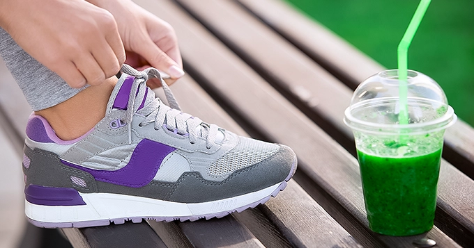 Someone tying their shoe on a bench with a green smoothie beside them | Trainest 